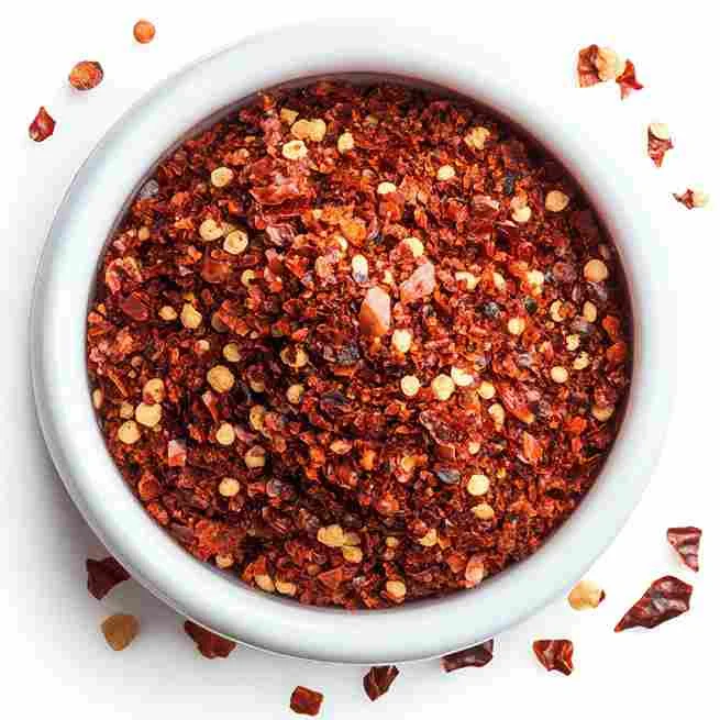 Close-up of artisanal crushed red pepper flakes in a wooden bowl, with dried chili peppers and spices on a rustic surface